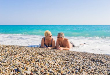 Orta yaşlı sevimli bir çift deniz kıyısında taştan bir plajda uzanıp birbirlerine mutlu bir şekilde bakıyorlar. Mutlu çift kumsalda birlikte yatıyor, yaşlılar deniz kenarında dinleniyor, aşk, yaşam tarzı....