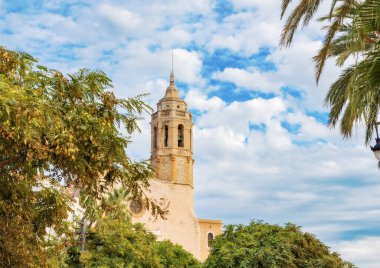 Mavi gökyüzü, palmiye ağaçları ve bitkilerin arka planında - Sitges, Katalonya, İspanya 'daki St. Bartholomew Kilisesi ve Santa Tecla manzarası