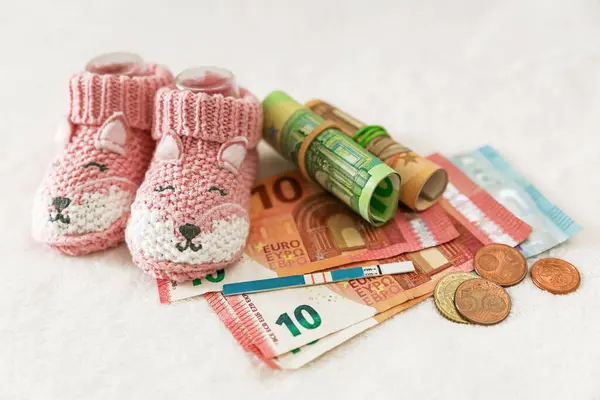 Hamilelik planı, annelik. Çocukların ördüğü çoraplar, hamilelik testi ve beyaz arka planda para. Çocuk parasının ödenmesi, pahalı çocuk kıyafetleri, aile bütçesi, gider planlaması.