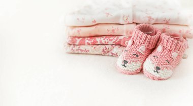 Bebek için küçük örülmüş ayakkabılar ve beyaz arka planda fotokopi alanı olan bebek kıyafetleri. Bir kızın doğumu için tebrikler. Hamilelik ve annelik kavramı, ilk doğum günü afişi..