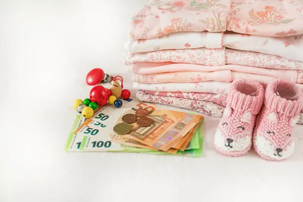 stock image Money, stack of baby clothes for a newborn on a white background with copy space. Pregnancy planning, motherhood. Family budget, children's money, child expenses.