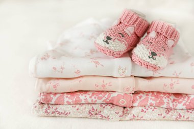 Bir bebek için küçük örülmüş ayakkabılar ve beyaz arka planda bir yığın bebek kıyafeti. Bir kızın doğumu için tebrikler. Bebeğe hediye. Hamilelik ve annelik kavramı, ilk doğum günü afişi..