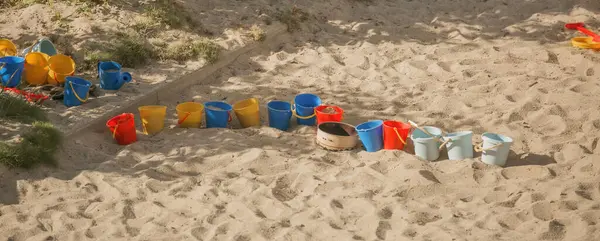 Anaokulundaki kum havuzunda oynamak için bir sürü renkli plastik çocuk kovası. Sıralama, kürek, çocuklar açık hava oyunu.