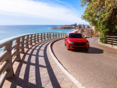 İspanya 'da öğlen vakti, deniz kıyısındaki köprüden geçen kırmızı araba. Avrupa yolları. Güneşten gelen gölgeler. Arabayla seyahat, yaşam tarzı.