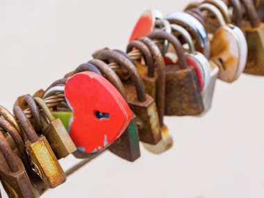 Köprüde pek çok farklı paslı kilit ve sonsuza dek sevgi ve sadakat sembolü olarak kalp şeklinde bir kırmızı kilit var. Düğün gelenekleri. Sevgililer Günü, yaşam tarzı.