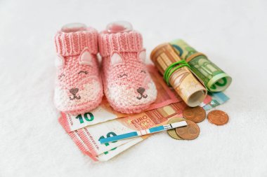 Nüfus sorunları. Para, hamilelik testi, beyaz arka planda bebek kıyafetleri, tüp bebek fiyatı, devlet çocuk yardımları, sağlık sigortası, artan doğum oranı.