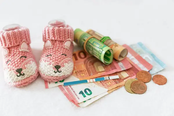 Para, hamilelik testi, beyaz arka planda bebek kıyafetleri, tüp bebek fiyatı, devlet çocuk yardımları, sağlık sigortası, nüfus sorunları, artan doğum oranı.