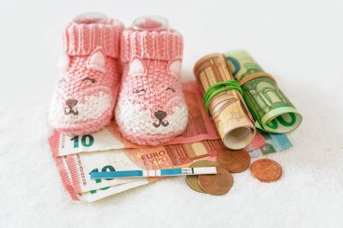 Hamileliği planlamak ve finanse etmek. Hamilelik testi, para, beyaz arka planda bebek kıyafetleri, tüp bebek fiyatı, devlet çocuk yardımları, sağlık sigortası, nüfus sorunları.