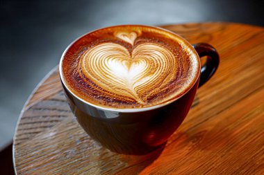 Latte art heart in black cup on wood.