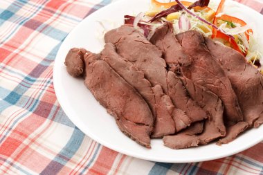 İnce dilimlenmiş soğuk biftek ve beyaz tabakta sebze salatası.