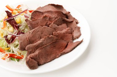 İnce dilimlenmiş soğuk biftek ve beyaz tabakta sebze salatası..