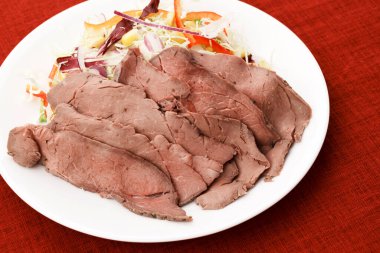 İnce dilimlenmiş soğuk biftek ve beyaz tabakta sebze salatası.