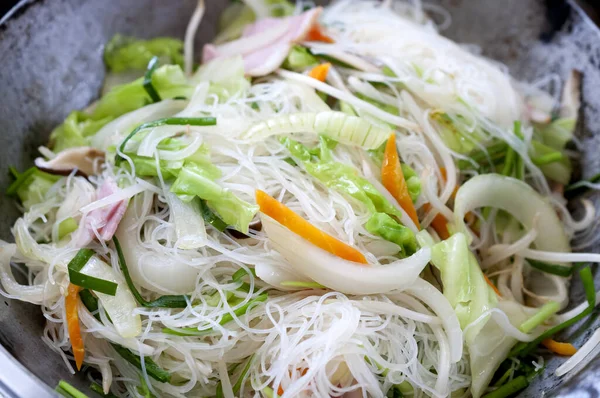 Cooking rice vermicelli with bacon and vegetables in a frying pan wok