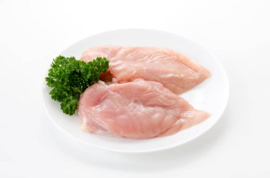 Beyaz arka planda maydanozlu çiğ tavuk göğsü.