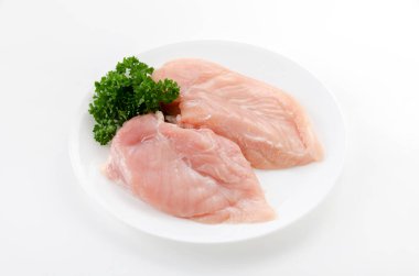 Beyaz arka planda maydanozlu çiğ tavuk göğsü.