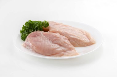 Beyaz arka planda maydanozlu çiğ tavuk göğsü.