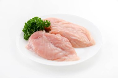 Beyaz arka planda maydanozlu çiğ tavuk göğsü.