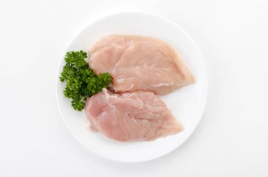 Beyaz arka planda maydanozlu çiğ tavuk göğsü.