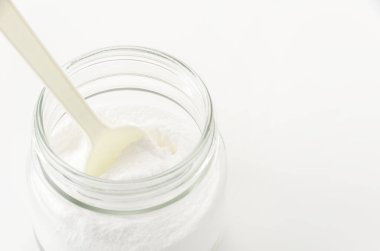 Cam kavanozda kabartma tozu ve beyaz arka planda plastik kaşık.