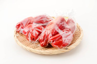 Kırmızı dolma biber plastik poşette beyaz arka planda bambu süzgeci