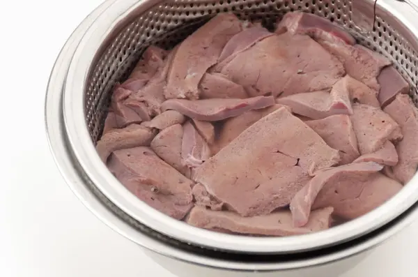 stock image Draining blood from pork liver in a stainless steel bowl filled with water on white background