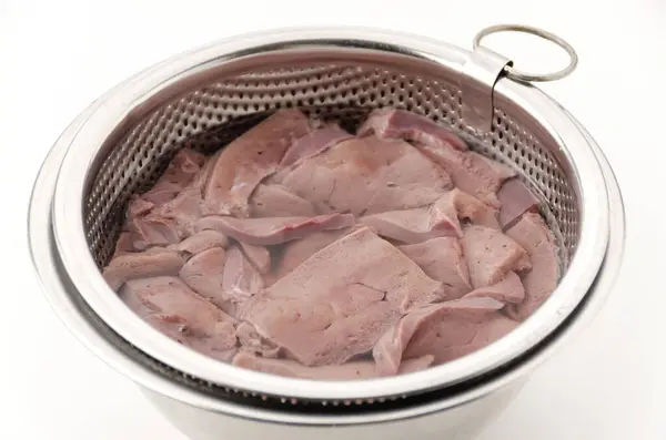 stock image Draining blood from pork liver in a stainless steel bowl filled with water on white background