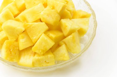 Beyaz arka planda şeffaf cam bir çanakta ananas parçaları.