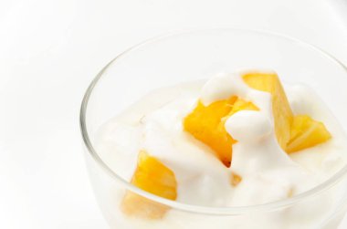 Beyaz arka planda ananas parçaları olan şeffaf cam yoğurt kasesi.
