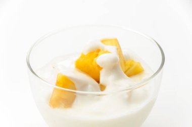 Beyaz arka planda ananas parçaları olan şeffaf cam yoğurt kasesi.