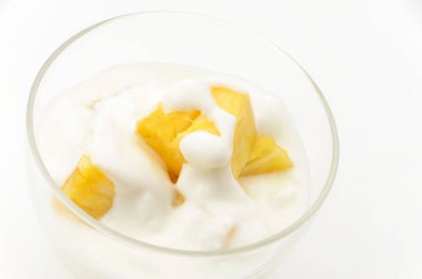 Beyaz arka planda ananas parçaları olan şeffaf cam yoğurt kasesi.