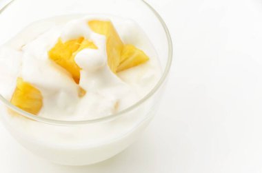 Beyaz arka planda ananas parçaları olan şeffaf cam yoğurt kasesi.