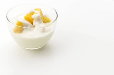 Beyaz arka planda ananas parçaları olan şeffaf cam yoğurt kasesi.