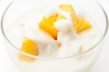 Beyaz arka planda ananas parçaları olan şeffaf cam yoğurt kasesi.