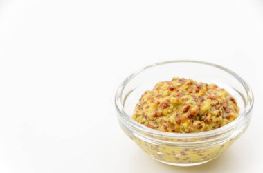 Beyaz zemin üzerinde küçük cam kâse içinde tam tahıllı hardal.