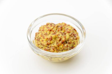 Beyaz zemin üzerinde küçük cam kâse içinde tam tahıllı hardal.