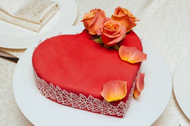 Kırmızı kalp şeklinde pasta, canlı güllerle süslenmiş bir şenlik masasında..