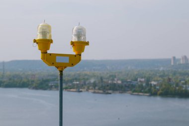 Uçak için sinyal lambaları. Yüksek bir binanın tepesinde uçak uyarı ışığı. Arka planda kasaba evleri olan nehir manzarası.