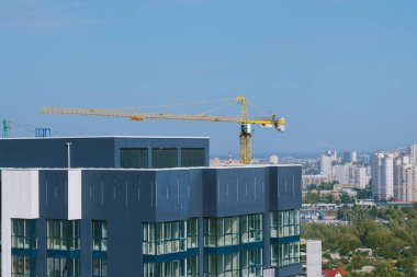 Gökdelenin en üst katında. İnşaat alanında sarı vinç ve bina var. Arka planda mavi gökyüzü ve şehir bölgelerine karşı vinç ve inşaat sahası.