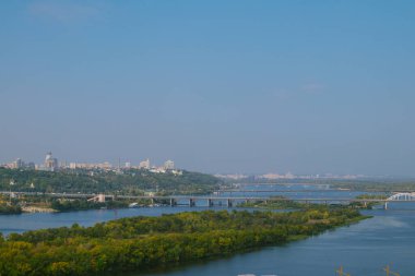 Nehrin ön planda yeşil ağaçlarla kaplı havadan manzarası ve arka planda şehir bölgeleri bulunan nehir üzerinde köprüler.. 