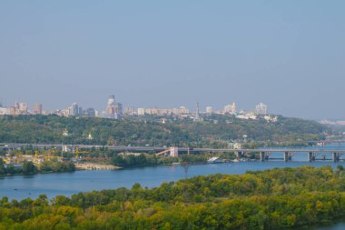 Nehrin yeşil ağaçlarla kaplı havadan görünüşü, ön planda ve şehir köprüsünde arka planda şehir bölgeleri var..