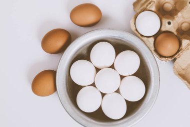 Parlak arka planda kahverengi yumurtalar. Metal kasede beyaz yumurta ve parlak arka planda kahverengi tepside yumurta. Yakın çekim, seçici odaklanma. Kavram sahnesi. Üst görünüm. 