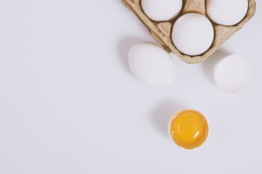 Yumurtanın yarısı kırılmış yumurta, yumurta tepsisinin yanında yumurta sarısı ve parlak bir arka plan. Seçici odaklanma. Kavram sahnesi. Üst görünüm