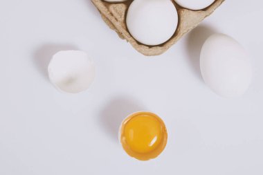 Yumurtanın yarısı kırılmış yumurta, yumurta tepsisinin yanında yumurta sarısı ve parlak bir arka plan. Seçici odaklanma. Kavram sahnesi. Üst görünüm