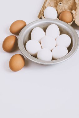 Parlak arka planda kahverengi yumurtalar. Metal kasede beyaz yumurta ve parlak arka planda kahverengi tepside yumurta. Yakın çekim, seçici odaklanma. Kavram sahnesi.. 