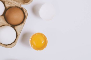 Yumurtanın yarısı kırılmış yumurta, yumurta tepsisinin yanında yumurta sarısı ve parlak bir arka plan. Seçici odaklanma. Kavram sahnesi. Üst görünüm