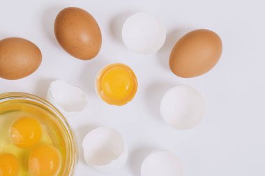 Kahverengi yumurtalar ve kırık beyaz yumurtalar. Yarısı cam kasenin içinde yumurta sarısı ve parlak arkaplanda yumurta akı var. Yaklaş, seçici odaklanma. Üst görünüm.
