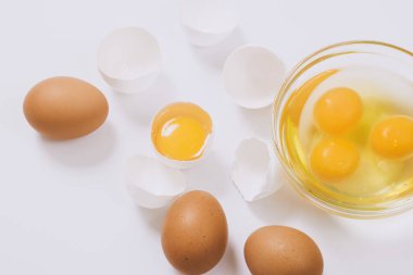 Kahverengi yumurtalar ve kırık beyaz yumurtalar. Yarısı cam kasenin içinde yumurta sarısı ve parlak arkaplanda yumurta akı var. Yaklaş, seçici odaklanma. 