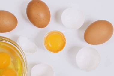 Kahverengi yumurtalar ve kırık beyaz yumurtalar. Yarısı cam kasenin içinde yumurta sarısı ve parlak arkaplanda yumurta akı var. Yaklaş, seçici odaklanma. Üst görünüm.