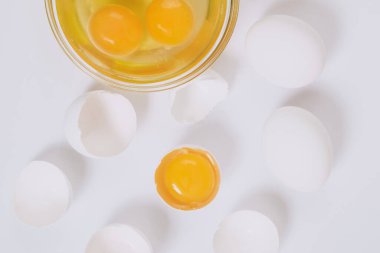 Tam beyaz yumurta ve kırık beyaz yumurta. Yarısı cam kasenin içinde yumurta sarısı ve parlak arkaplanda yumurta akı var. Yaklaş, seçici odaklanma. Üst görünüm.