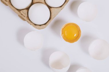 Yumurtanın yarısı kırılmış yumurta, yumurta tepsisinin yanında yumurta sarısı ve parlak bir arka plan. Seçici odaklanma. Kavram sahnesi. Üst görünüm